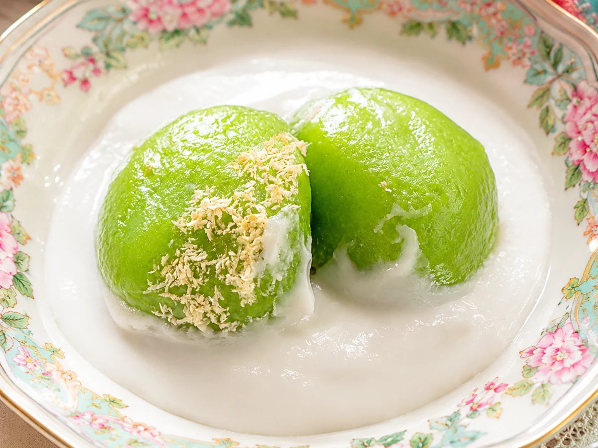 Kue Putri Mandi kenyal berwarna hijau dalam mangkuk berisi kuah santan putih gurih